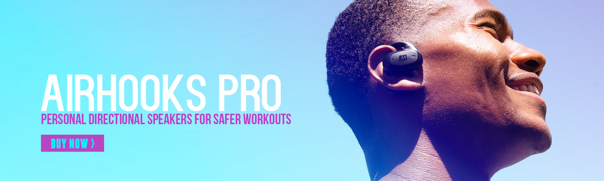A close-up side profile of a smiling man wearing Airhooks PRO earphones against a bright blue background, with text advertising "airhooks pro" personal directional speakers for safer workouts and a "buy now" option