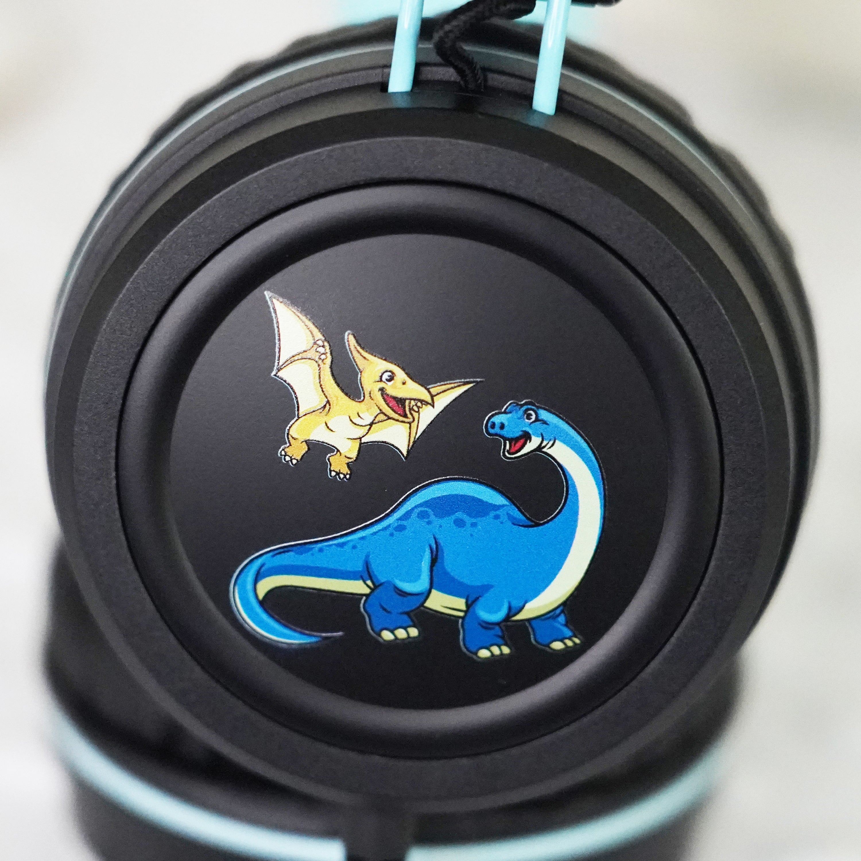 Black KidJamz KJ55AUX headphones faceplate with a cartoon dinosaur design in color on a light gray background