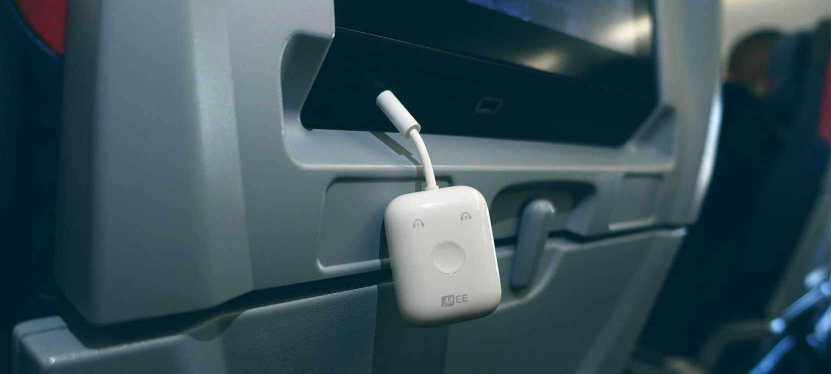 A bluetooth travel adapters plugged into a plane's inflight entertainment system, hanging from the back of an airplane seat, to enable movie watching during a flight.
