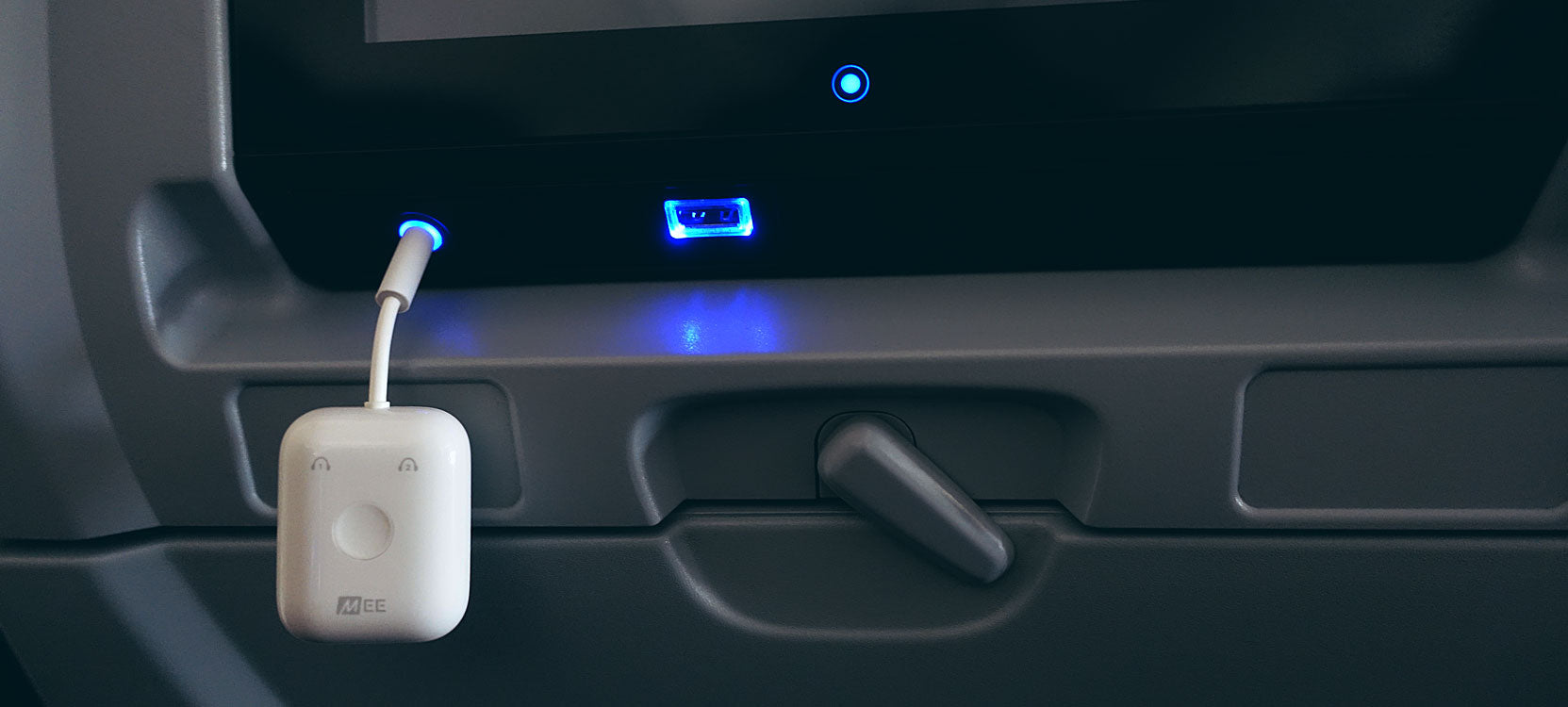 mee audio connect air bluetooth travel adapters transmitter emitting a blue light plugged into a plane's in flight dashboard usb port, indicating connectivity or activity.