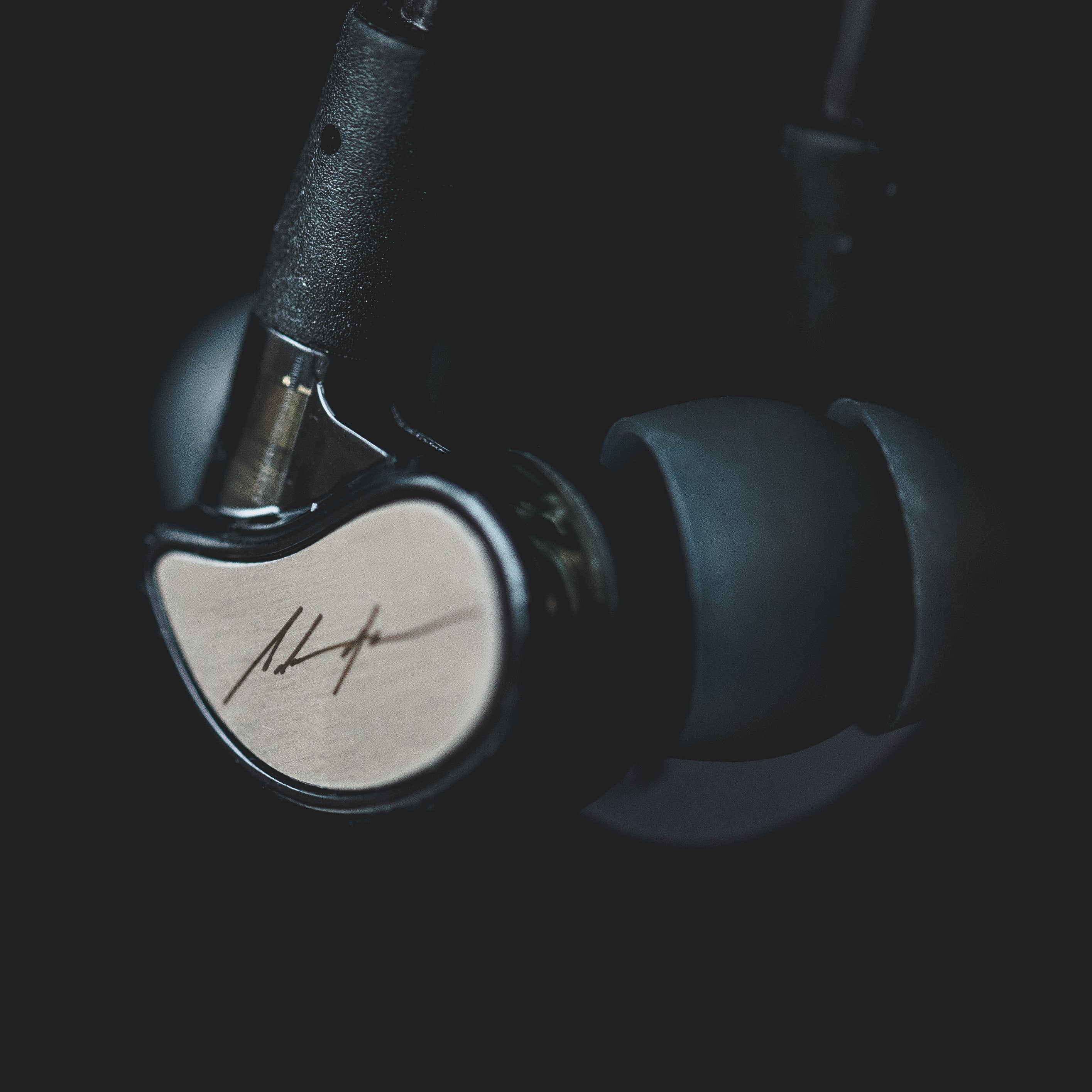Close-up of a pair of earphones with metallic details and a signature on the earpiece, set against a dark background.