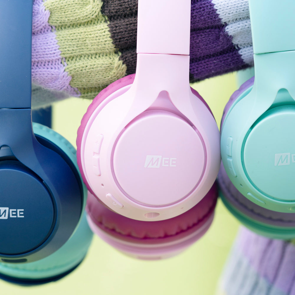 Three colorful mee headphones in blue, pink, and green, each with cushioned ear pads, displayed against a pastel striped background.