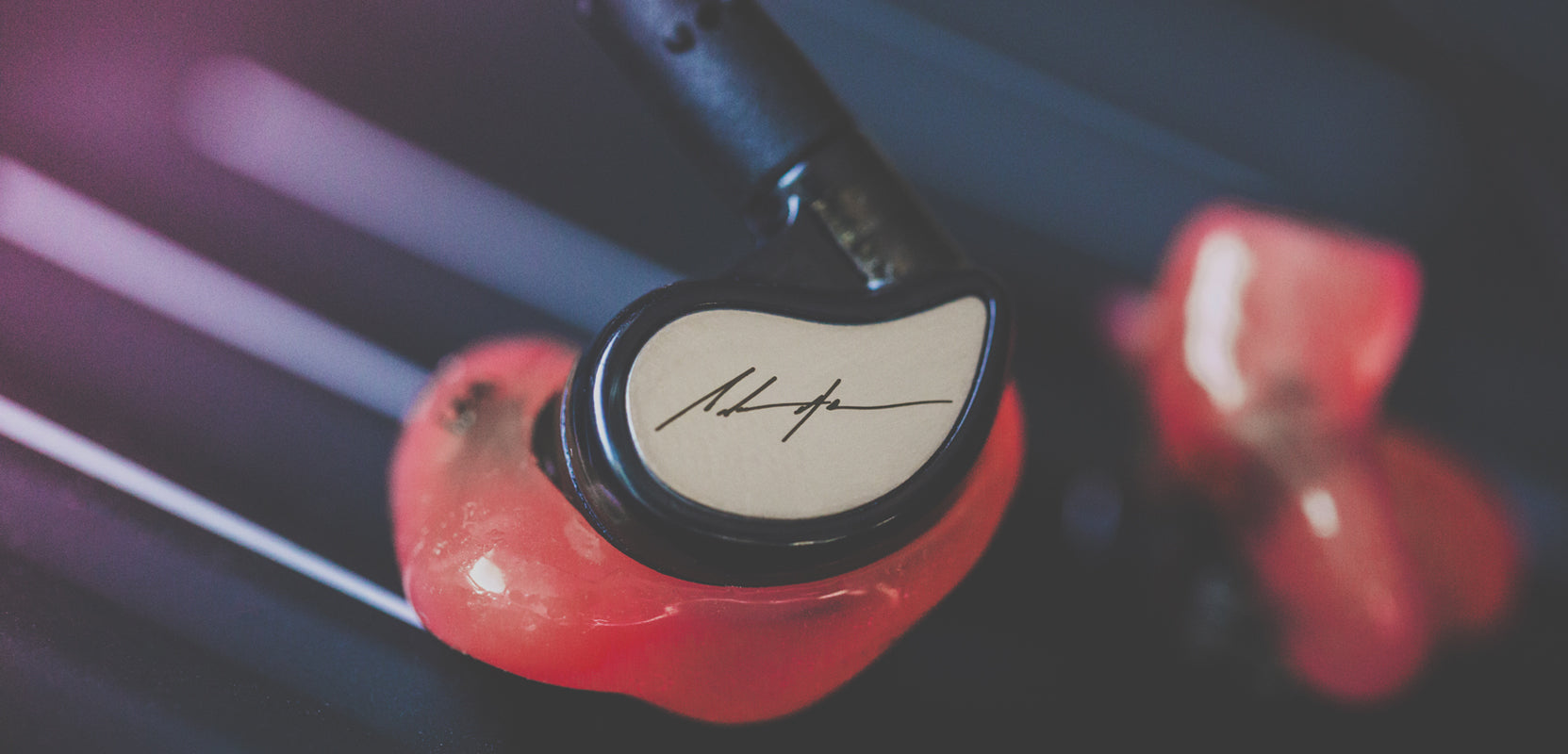 Close-up image of a pair of custom red in-ear monitors with a signature design on the faceplate, placed on a dark background with soft lighting.
