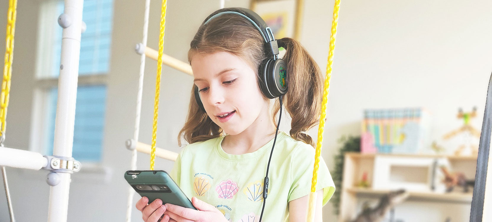 Young girl with Black KJ55AUX headphones using a smartphone on a swing