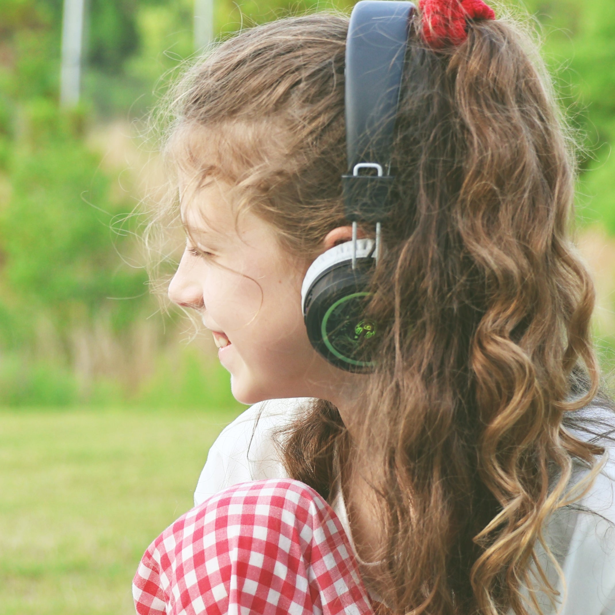 Girl wearing MEE audio KidJamz Share Bluetooth Wireless Headphones for Kids with Multipoint, LED Lights, 85dB Volume Limiter, Microphone, 40h battery; Childrens Headset for School/iPhone/iPad/Tablet in a park setting