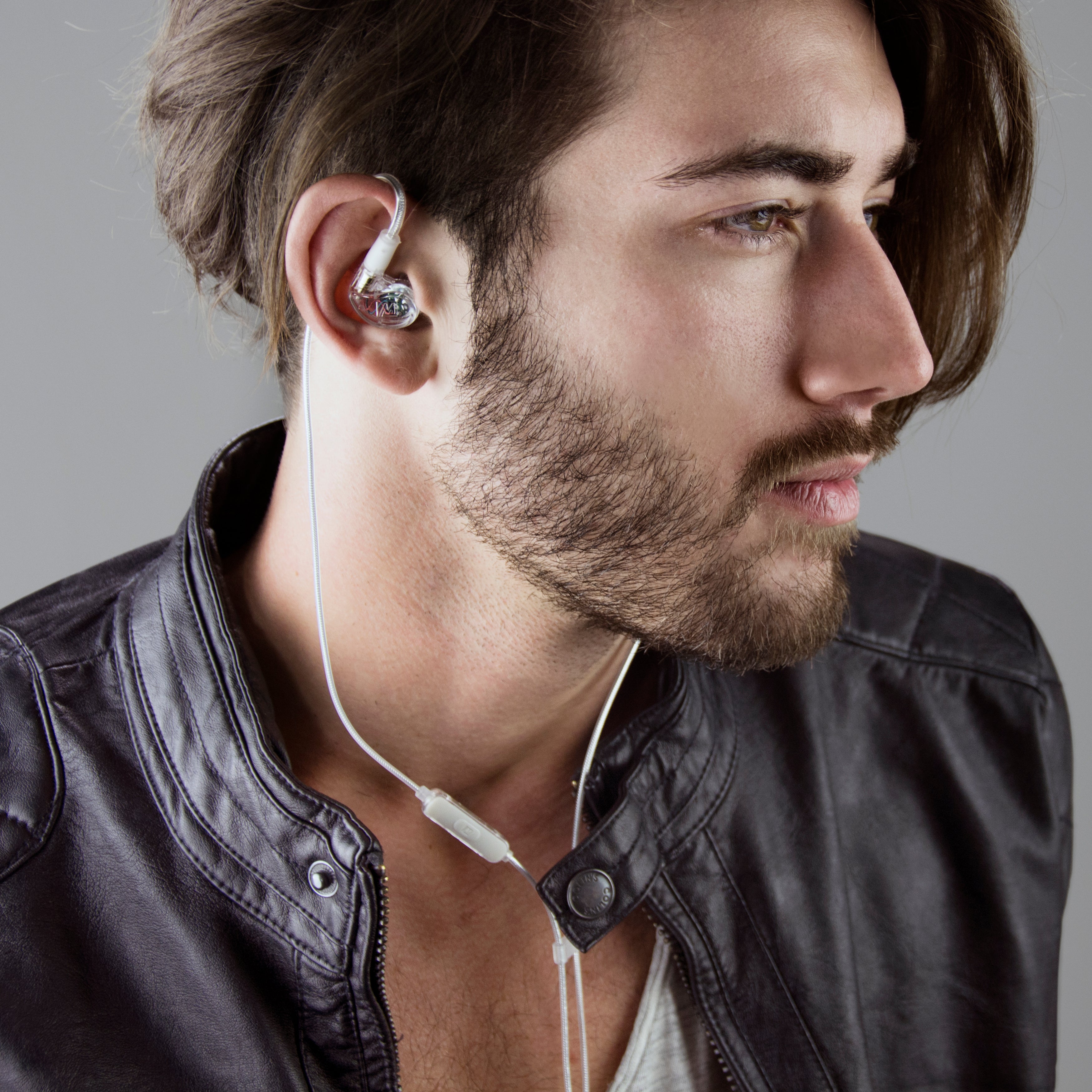 A side profile of a young man with a beard, wearing a leather jacket and white earphones, looking thoughtfully to the side.