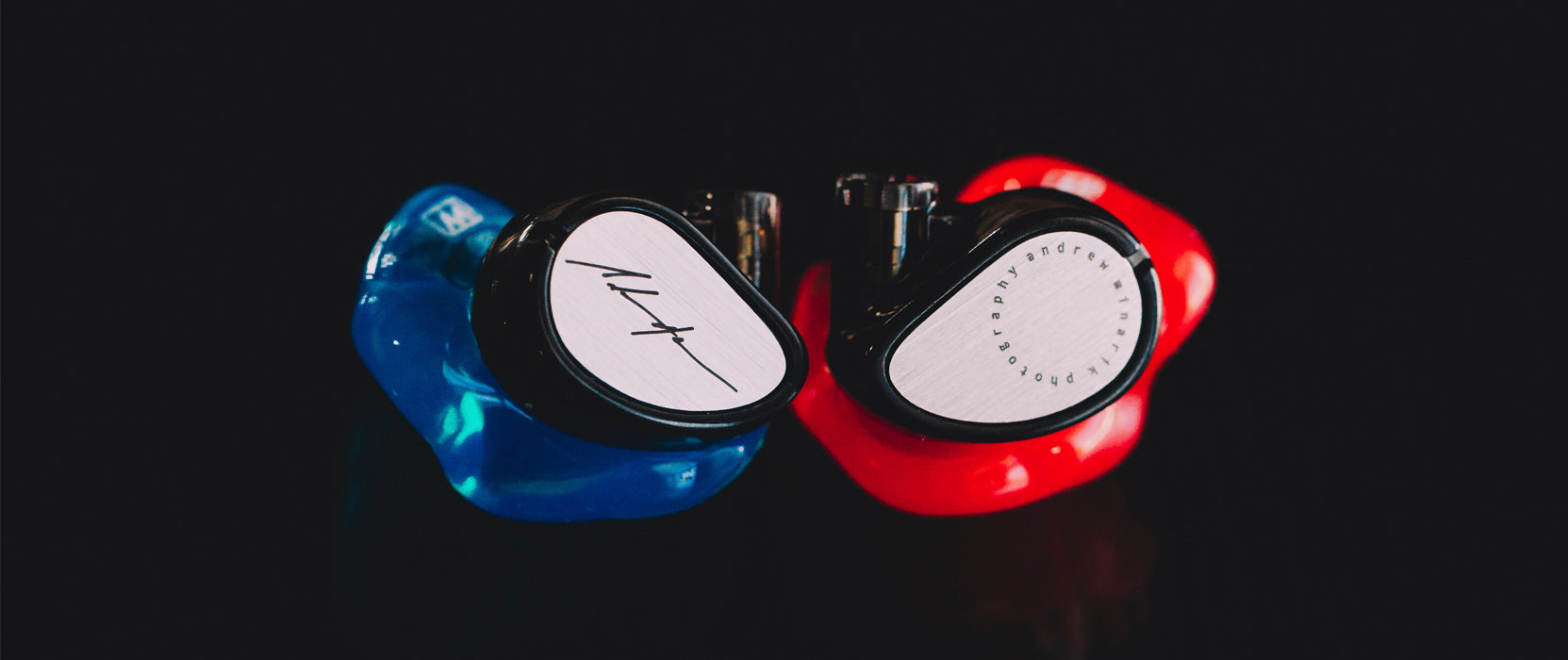 Two custom in-ear monitors, one red and one blue, with white faceplates featuring logo engravings, set against a black background.