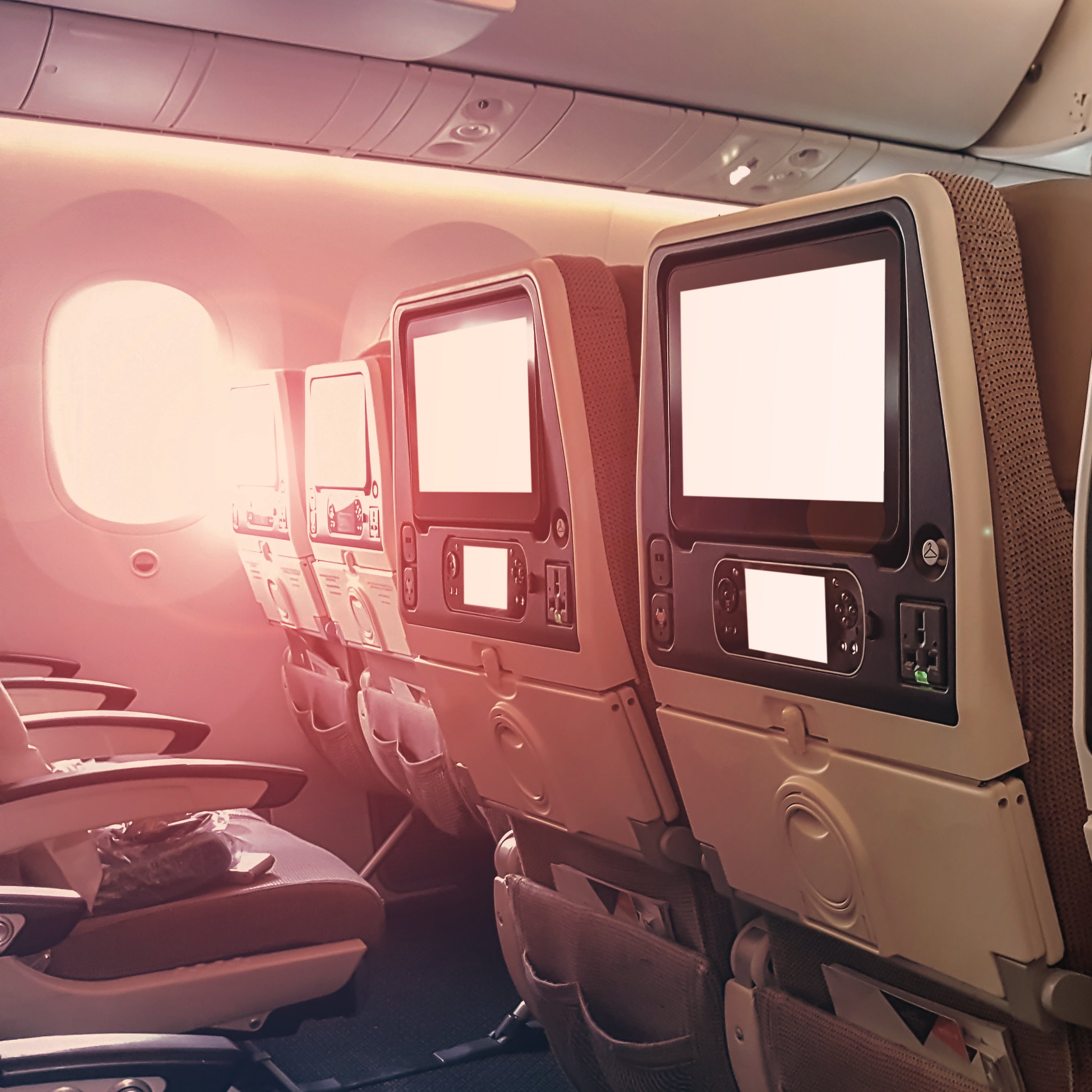 Row of airplane seats with entertainment screens on a dimly lit plane.