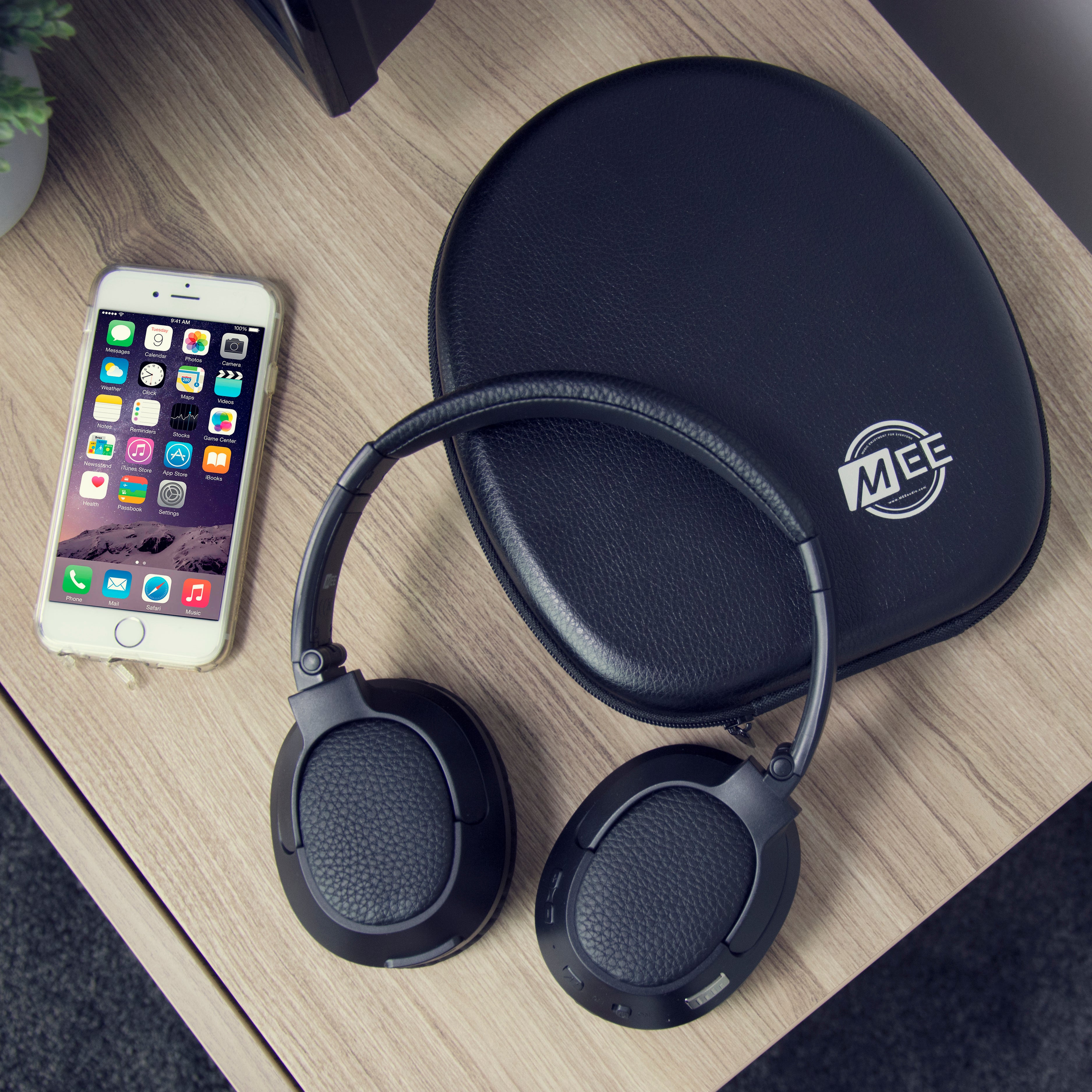 A smartphone displaying colorful app icons lies next to black headphones and a carrying case on a wooden table.