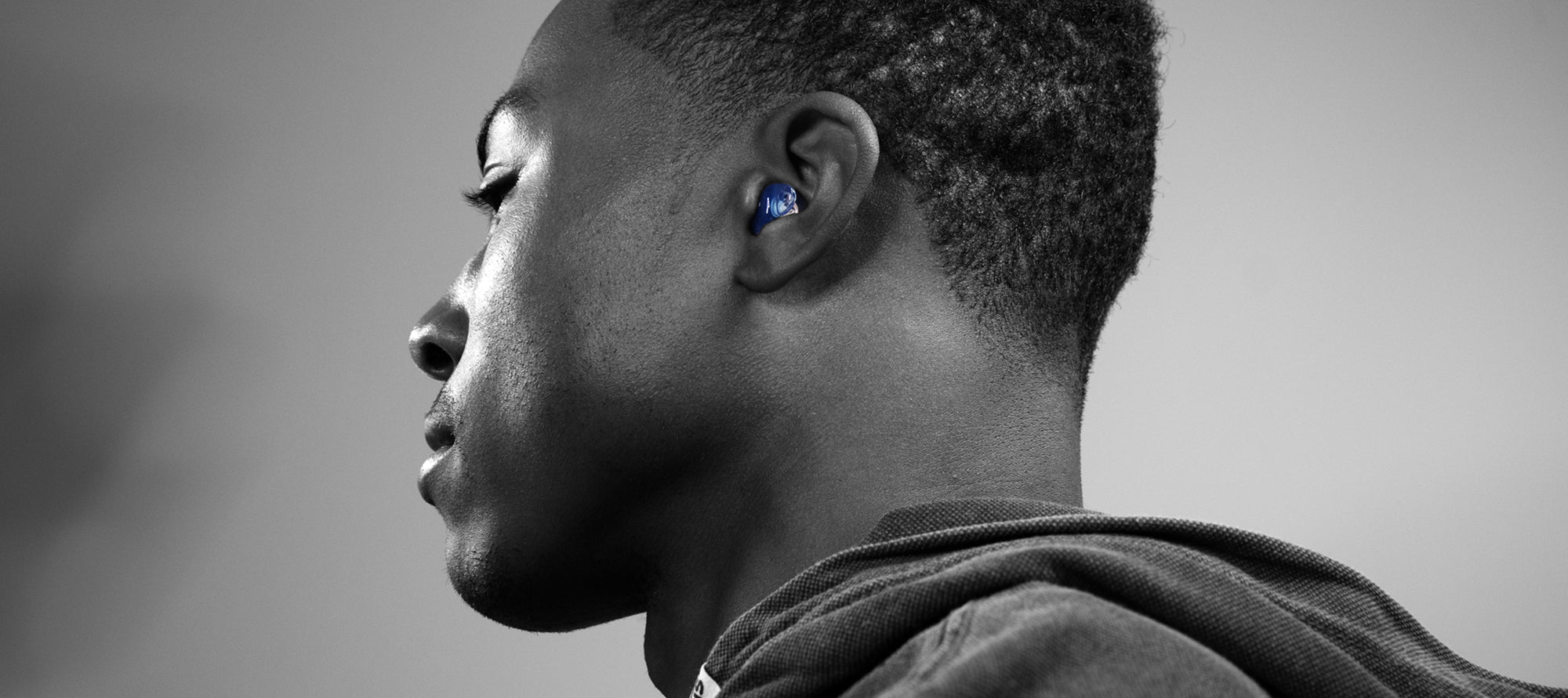 Profile of a young man wearing wireless earbuds, shot in black and white, focusing on his ear and the side of his face.
