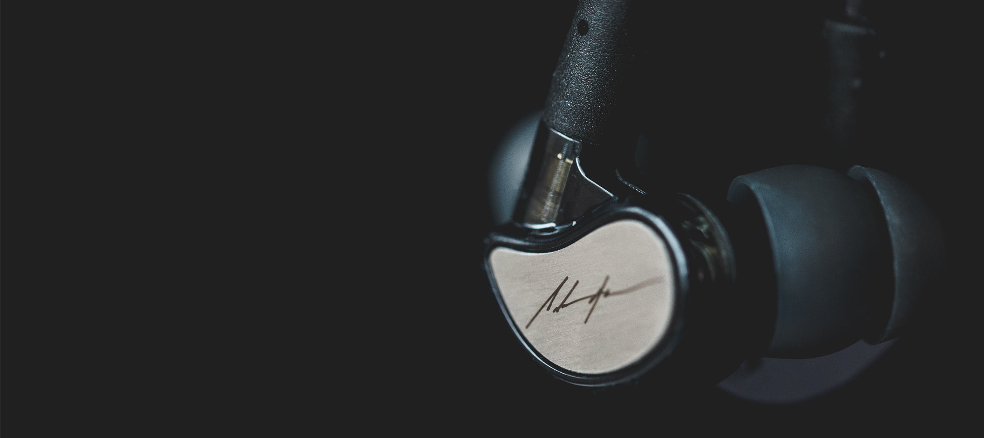 Close-up of an earbud with a metallic finish and a signature on its side, set against a dark background. the focus is sharp on the earbud, highlighting its sleek design.