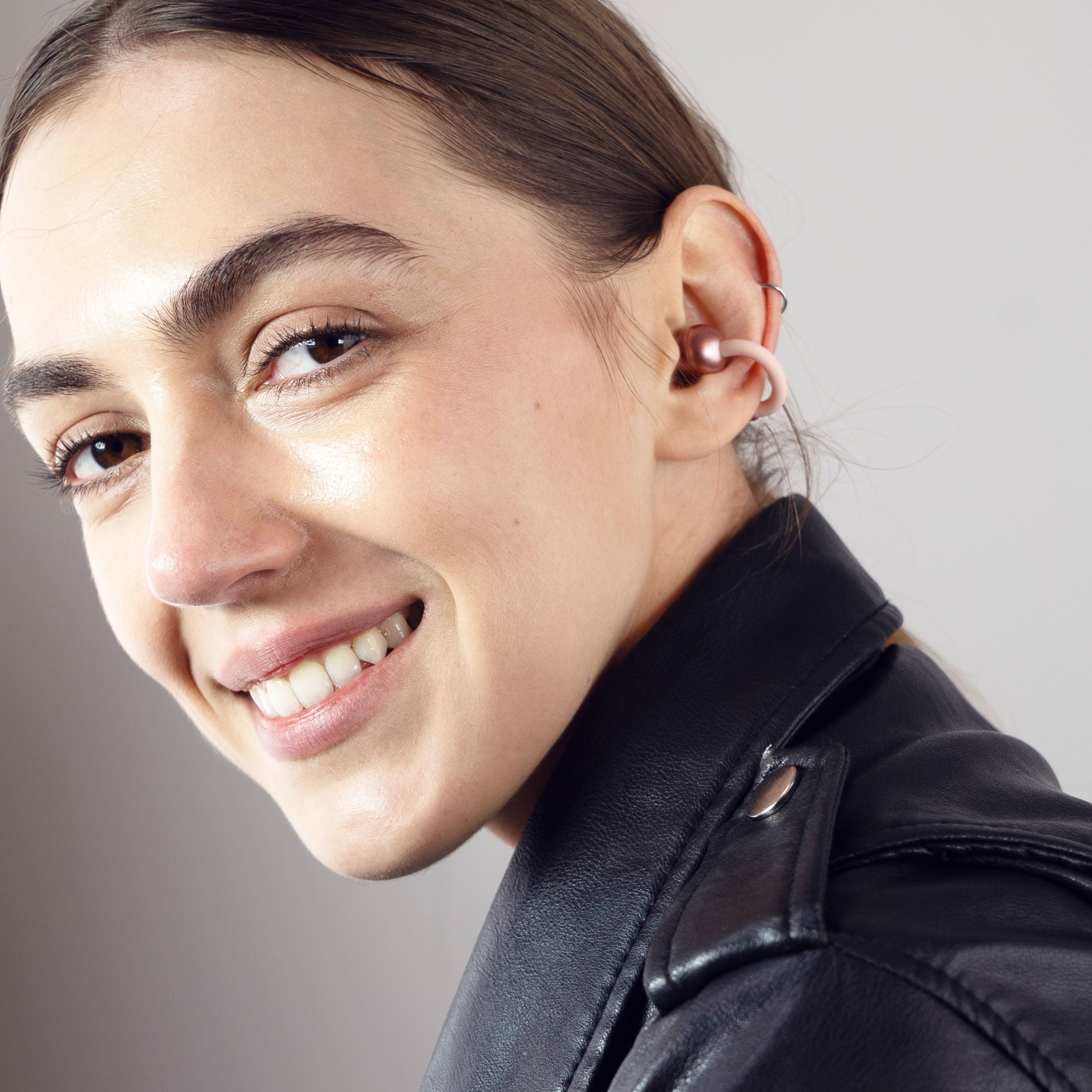 Close-up of a woman wearing pink Pebbles Air earbuds with a neutral background