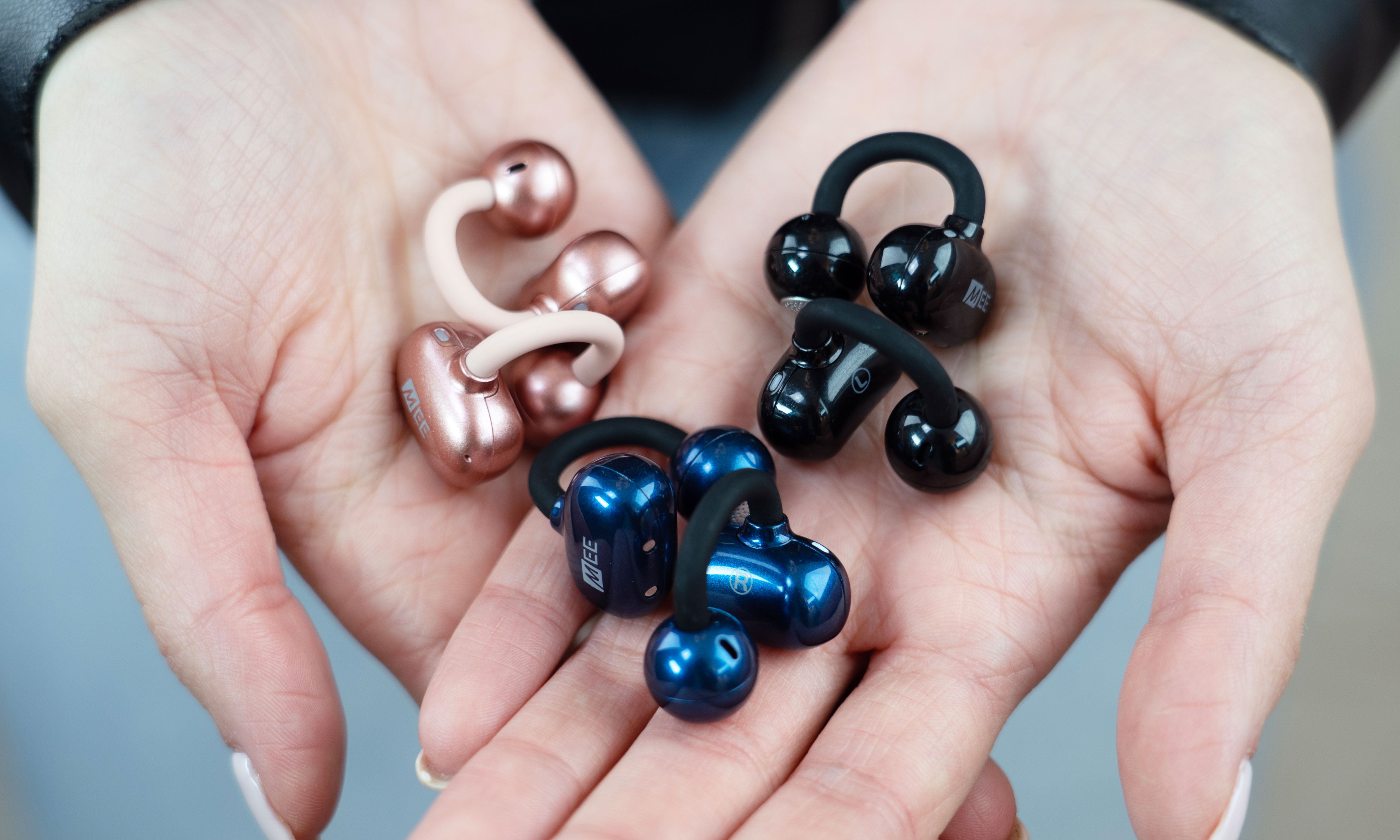 Hands holding multiple Pebbles Air earbuds in various colors.