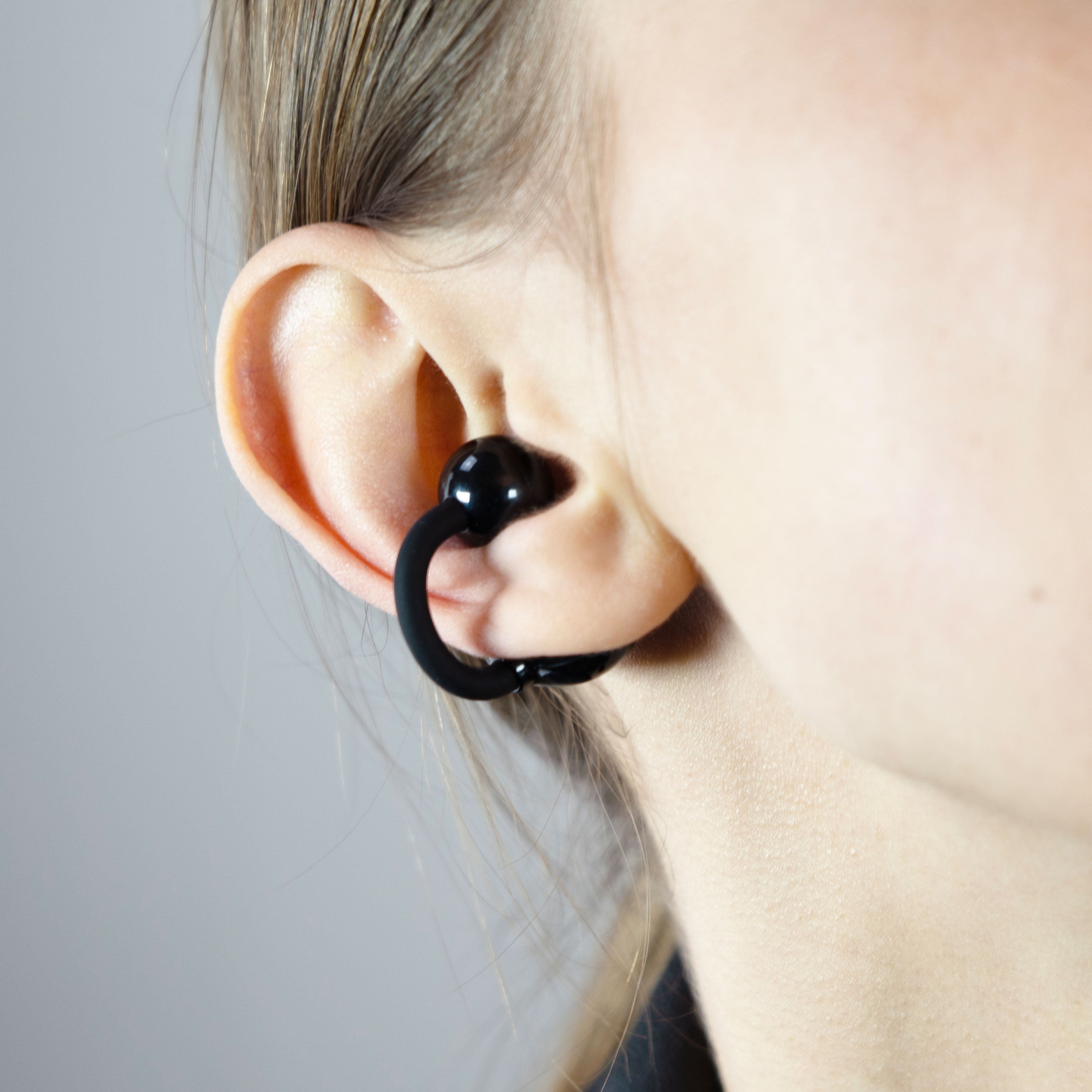 Close-up of an ear wearing a black Pebbles Air earbud against a neutral background