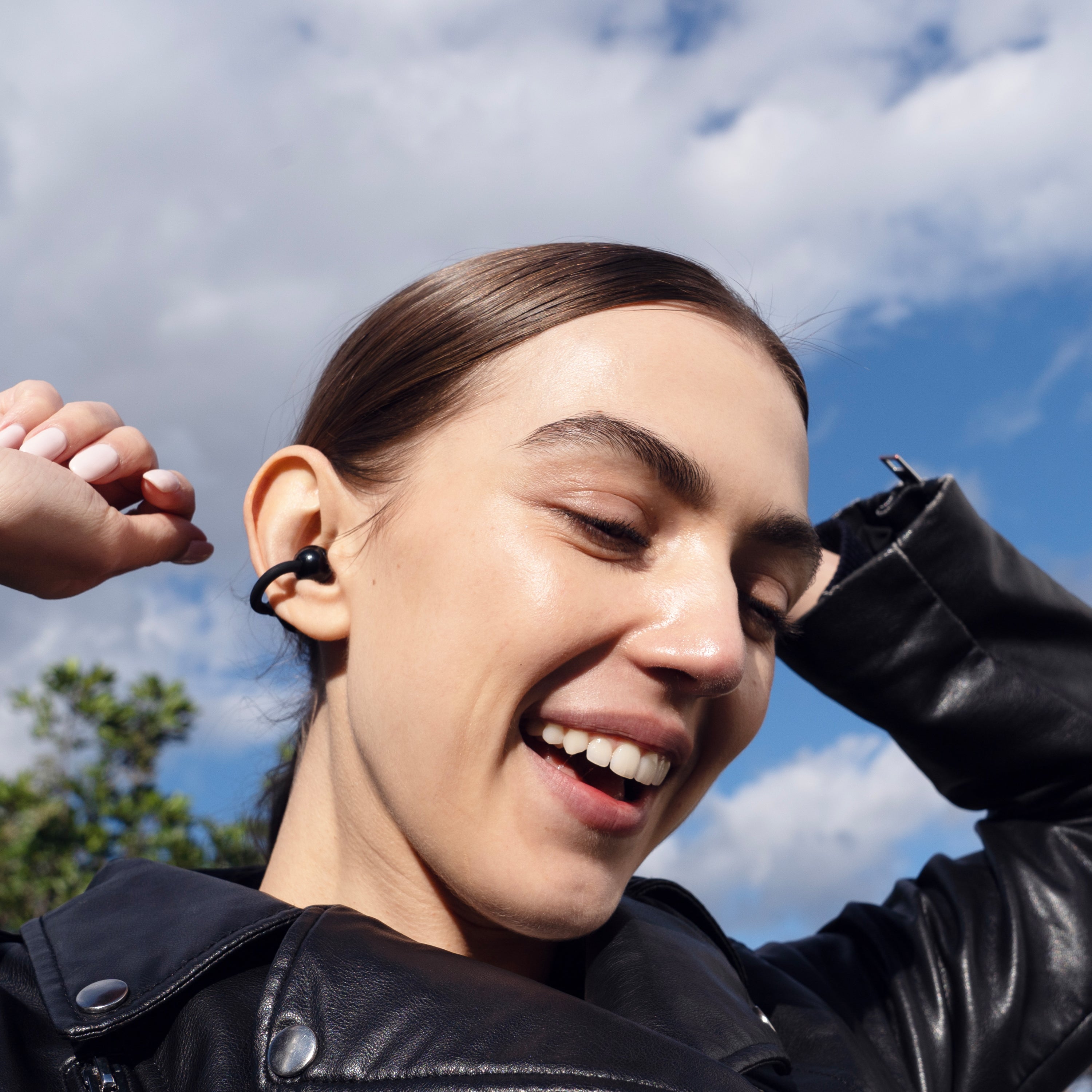 Person wearing a black Pebbles Air earbud with a blue sky and clouds in the background