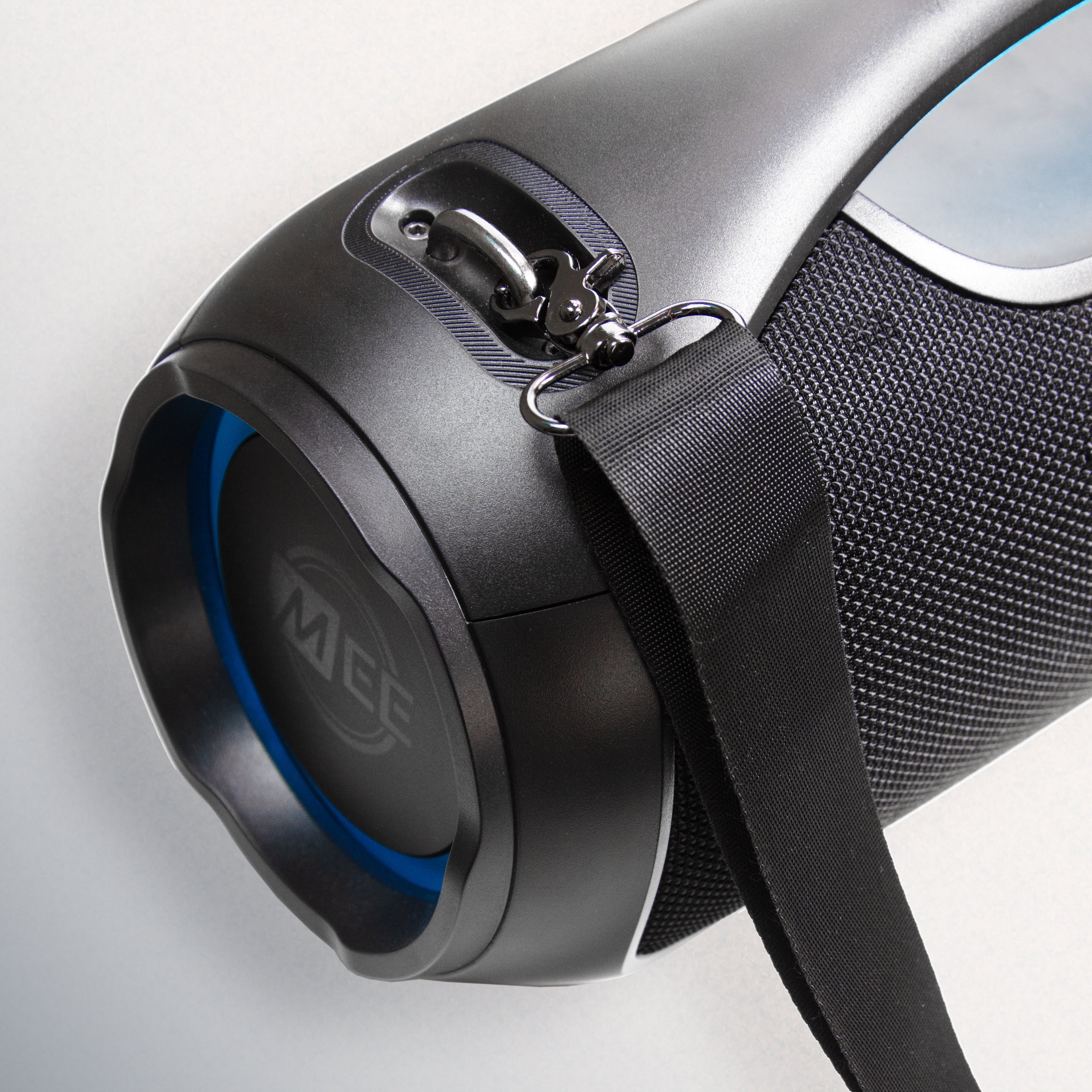 Close-up of a black portable speaker with a fabric strap and a blue accent around the speaker port. the brand name 'meg' is visible on the blue accent.