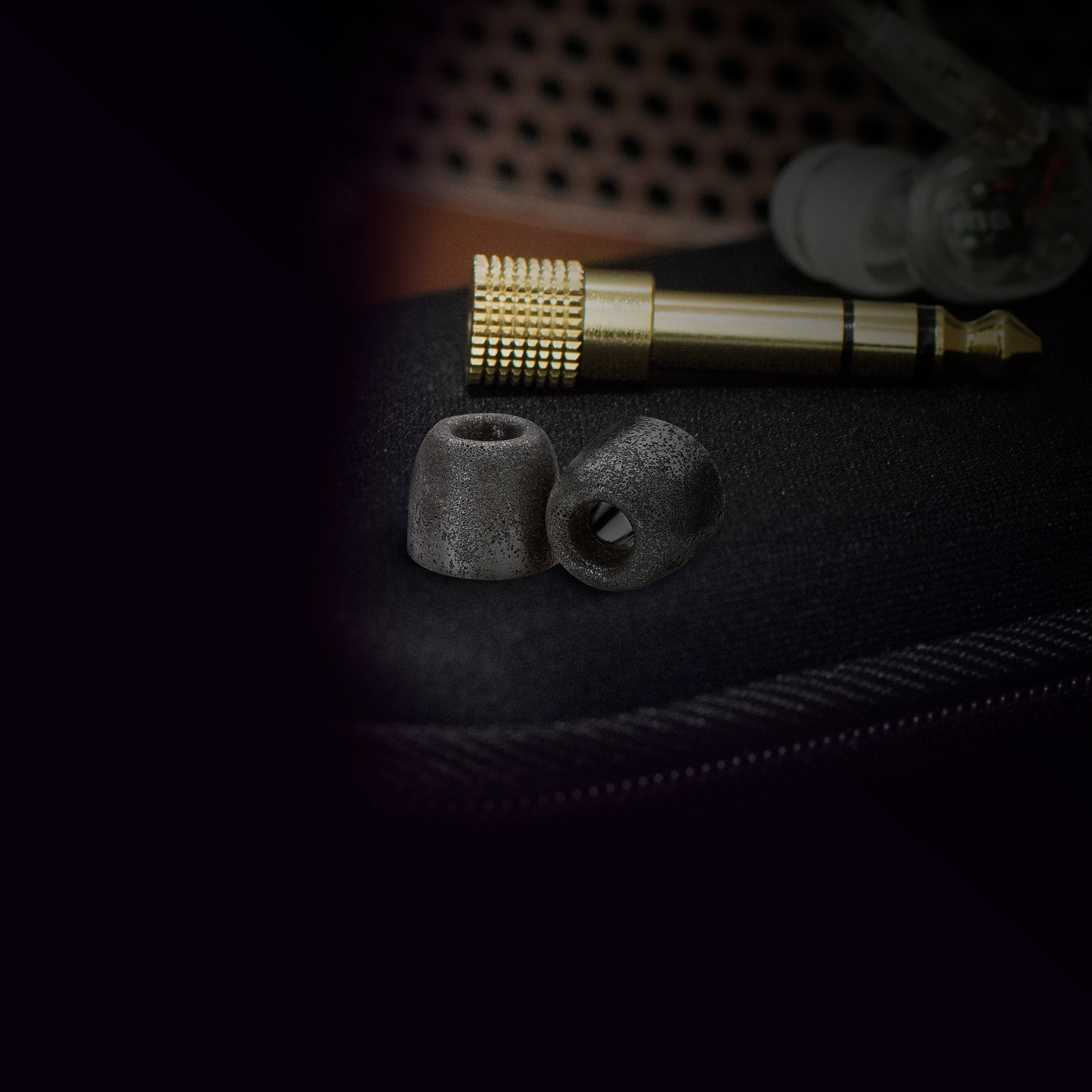 Close-up of a headphone jack and earbud tips on a dark textured surface, highlighting the metallic and rubber parts with a soft-focus background.