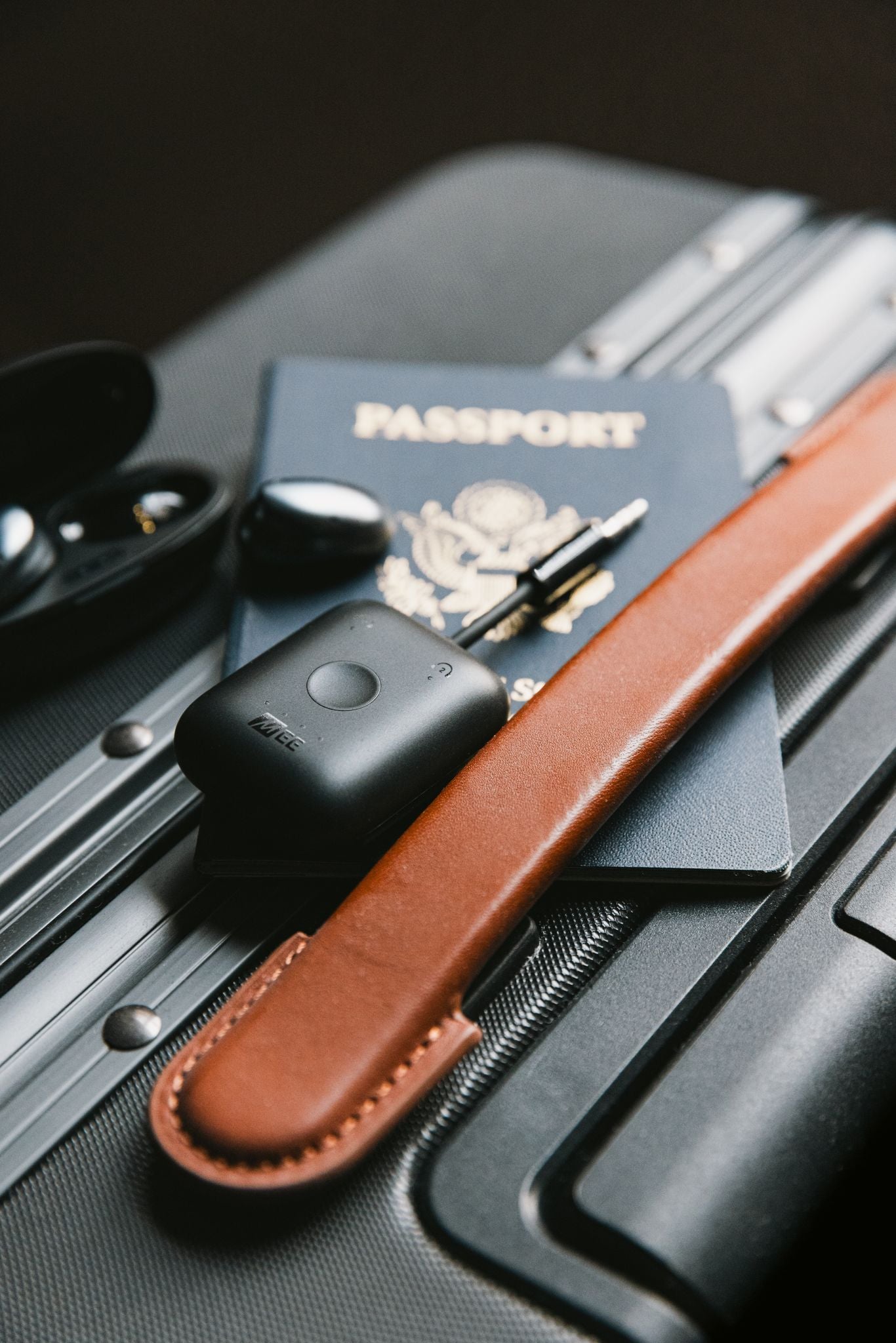 A close-up of travel essentials including a MEE Audio Connect Air Bluetooth adapters, US Passport, sunglasses, Pebbles earphones on a travel suitcase.