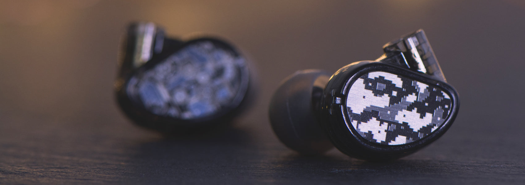 Close-up view of two wireless earbuds with digital camouflage patterns on the exterior, resting on a dark wooden surface.