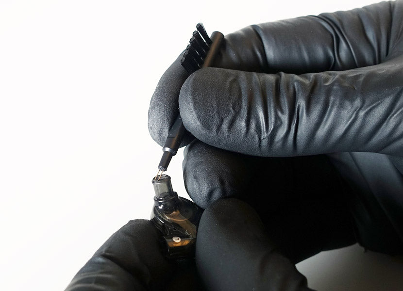 Close-up of two hands wearing black gloves, using a screwdriver to adjust or repair a small electronic device against a white background.