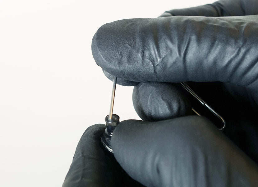 A person wearing black gloves is meticulously handling a small electronic component with tweezers against a white background.