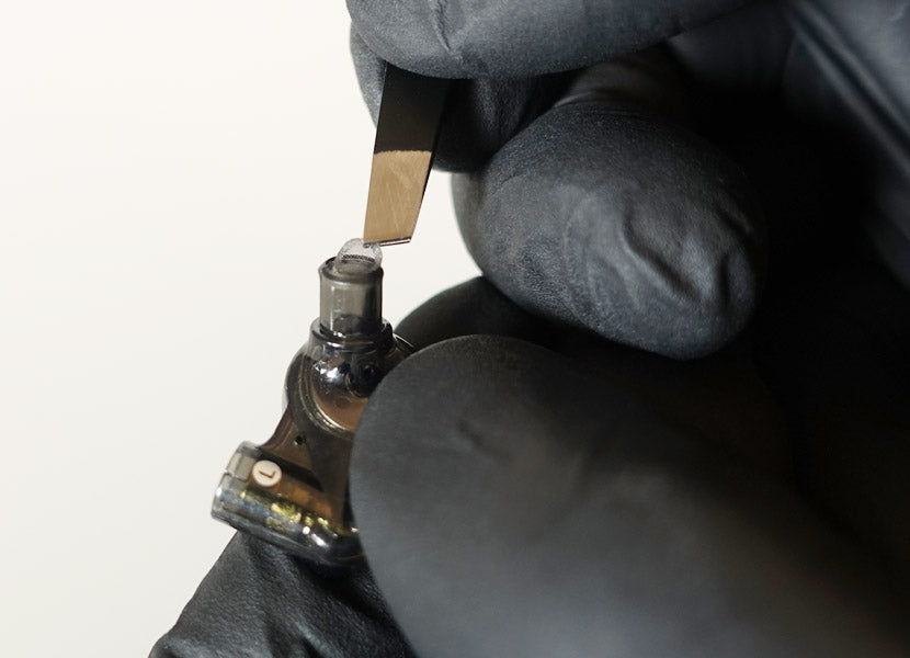 Close-up of a person in black gloves handling a small glass bottle with a pipette, against a neutral background.