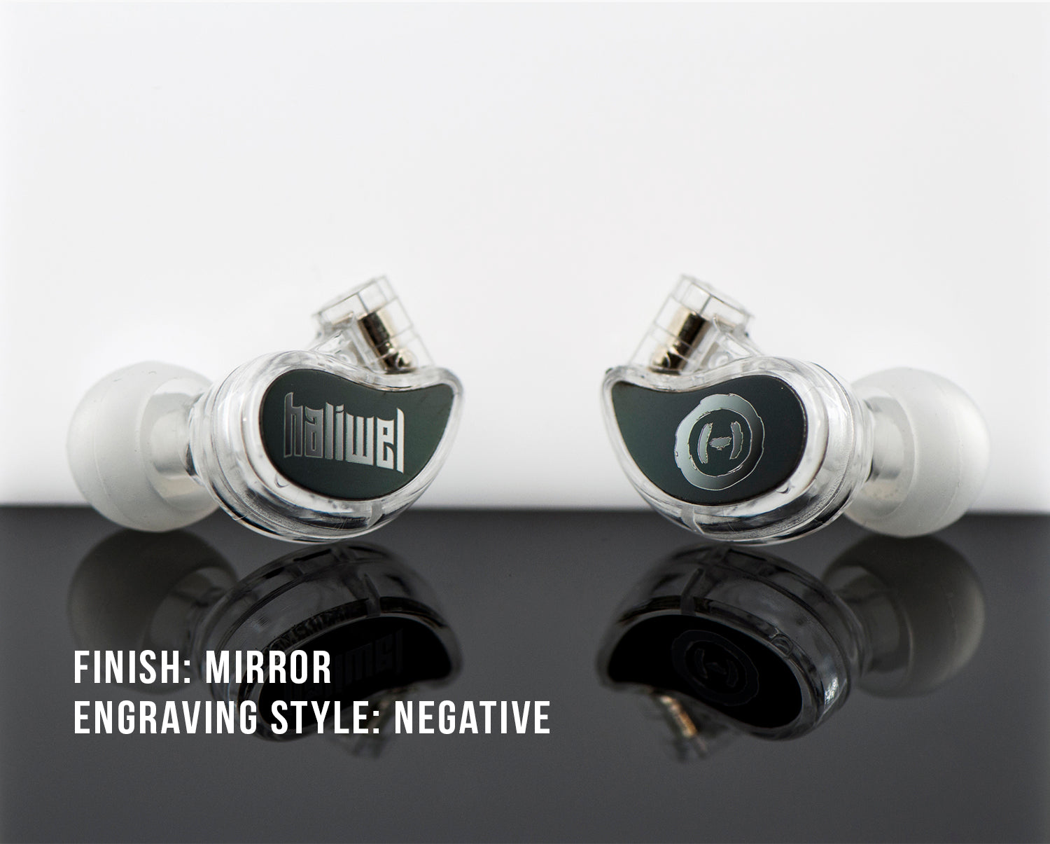 Two custom in-ear monitors with a mirror finish and negative engraving, displaying logos, reflected on a shiny surface with text descriptions.