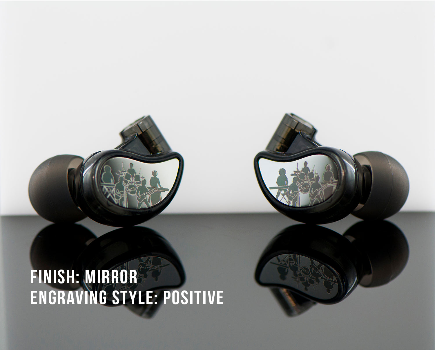 Two black, mirrored-finish in-ear monitors with an engraved design featuring multiple figures, displayed on a reflective surface against a light background. text labels state "finish: mirror" and "engraving style: positive.