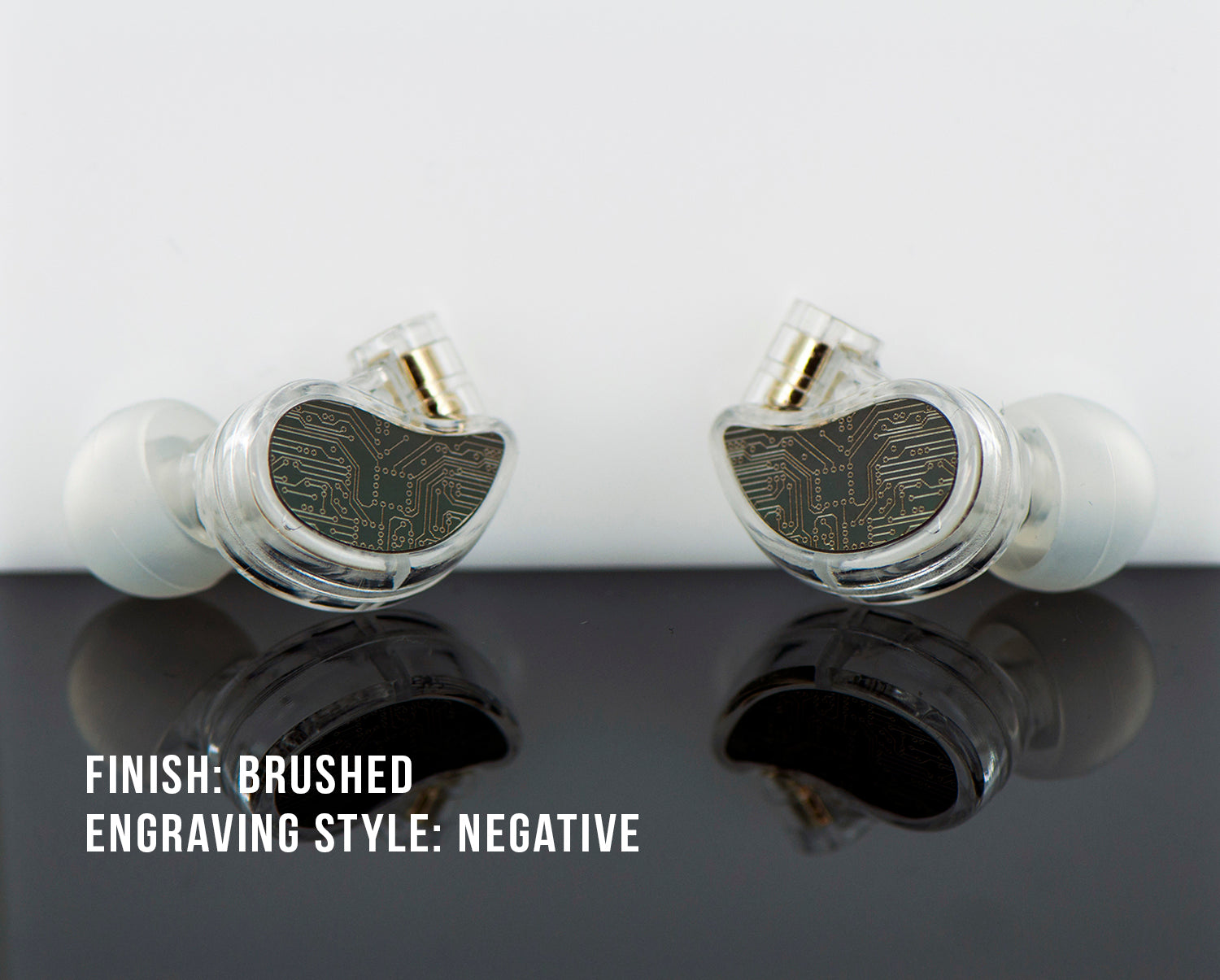 Two high-end in-ear monitors with brushed finishes and negative engraving styles of circuit patterns, displayed atop a reflective surface against a white background.