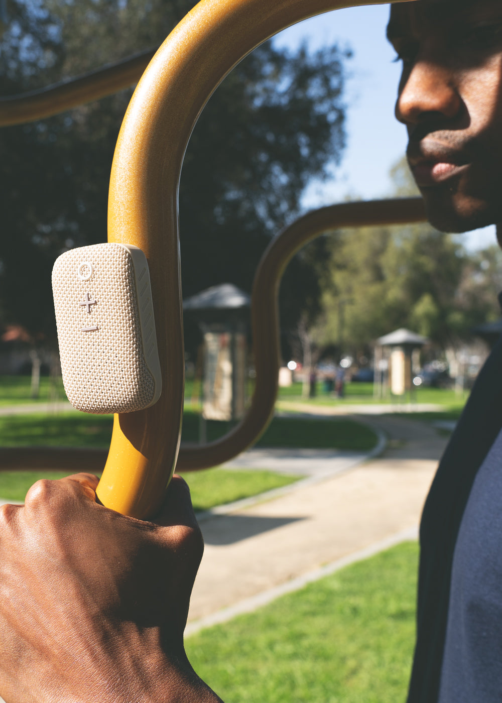 A close-up view of a black man holding onto a yellow curved metal bar of outdoor exercise equipment, focusing intently on holding the handle.