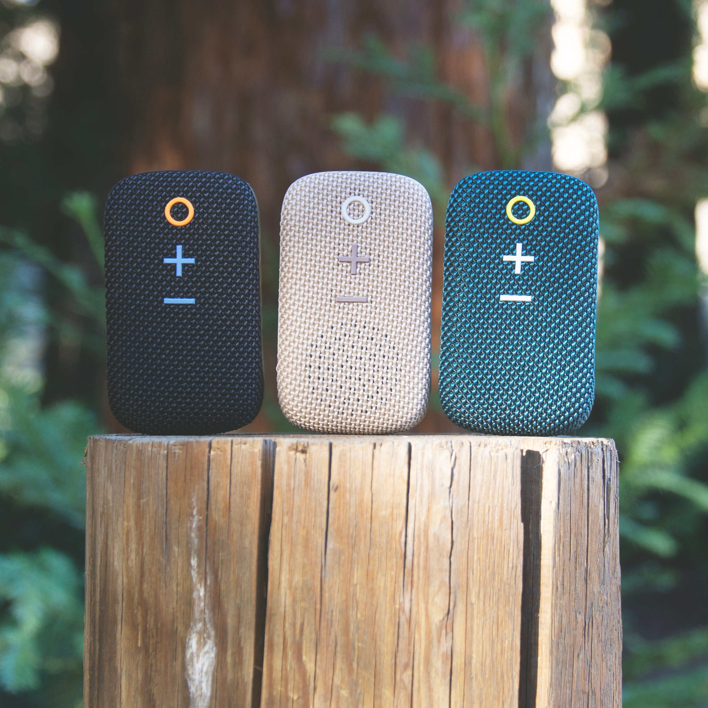 MEE audio goSPKR Wearable Clip-on Bluetooth Speaker in Black, Beige and Teal on a wood log outdoors