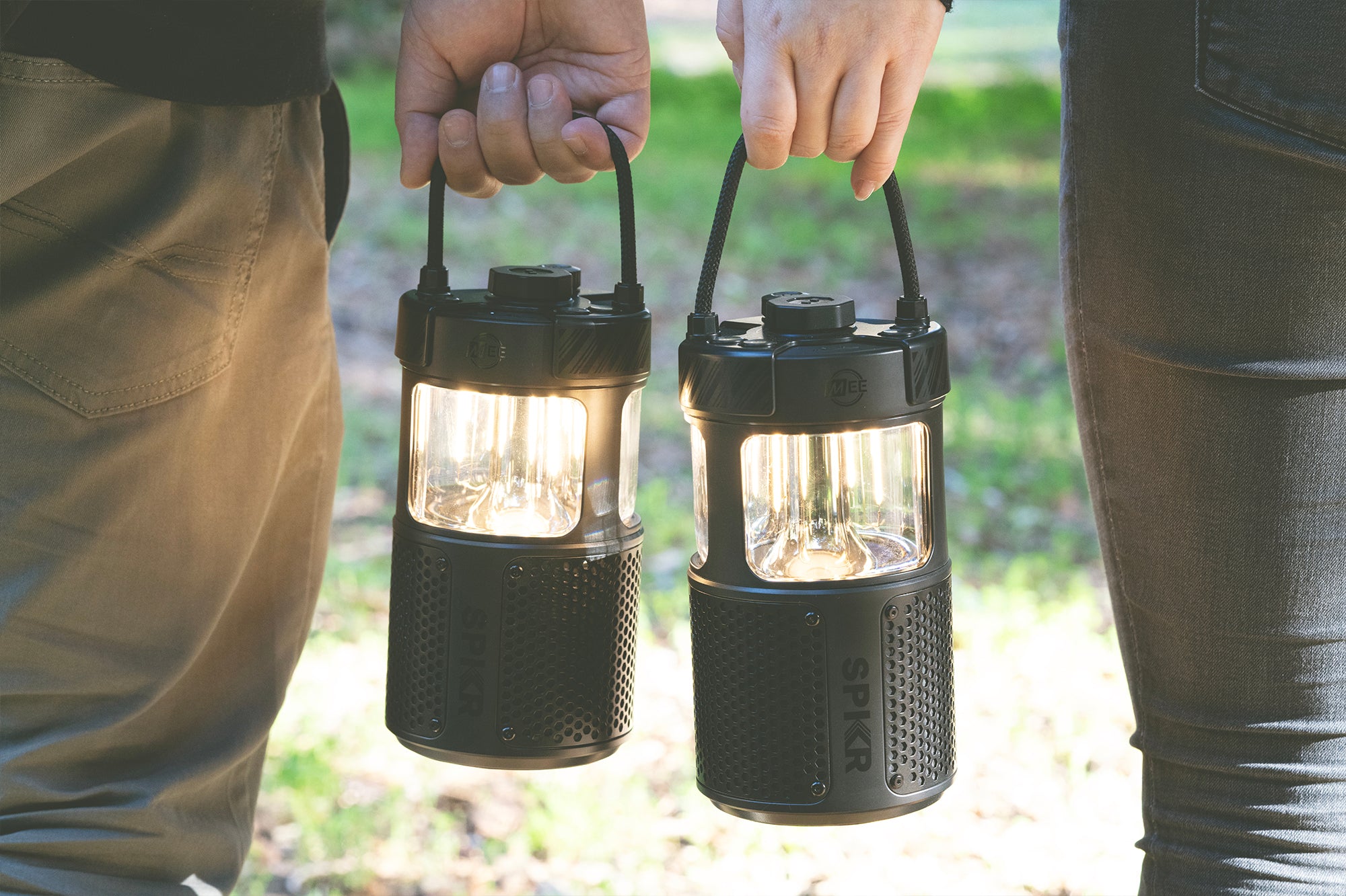 Two people standing outdoors, each holding a portable led camping lantern by the handle, showcasing the design and functionality of the lanterns in a natural setting.