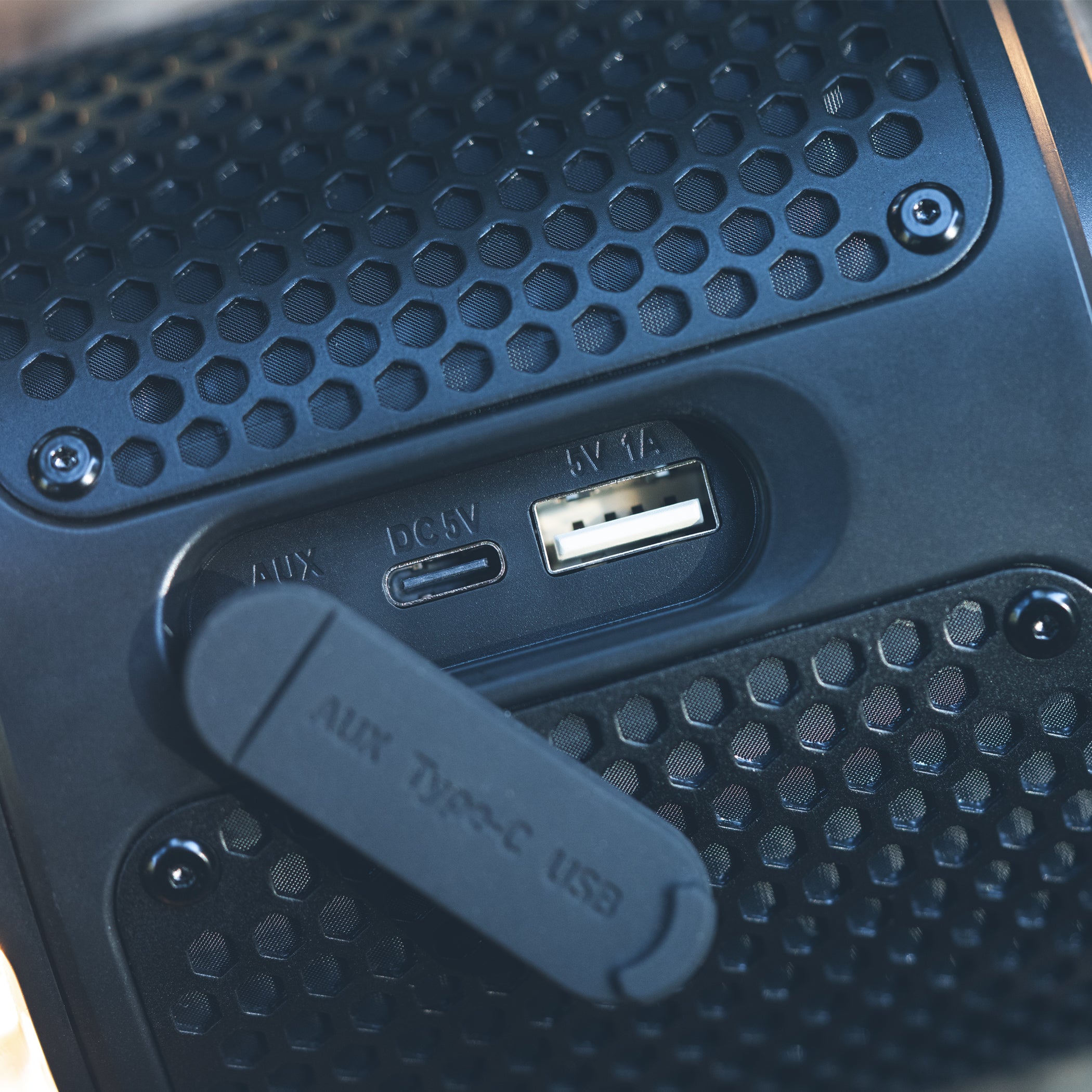 Close-up of a portable speaker's back panel showing an auxiliary input, dc 5v port, and a usb port, all set within a black honeycomb grille texture.