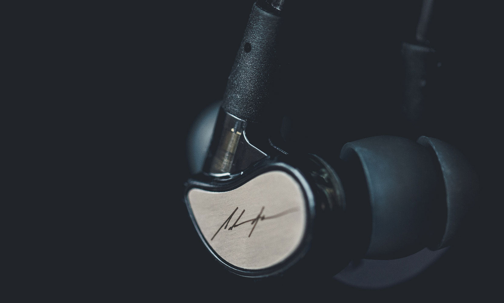 Close-up of a pair of black in-ear headphones with a sleek metallic finish and a visible logo, set against a dark background.