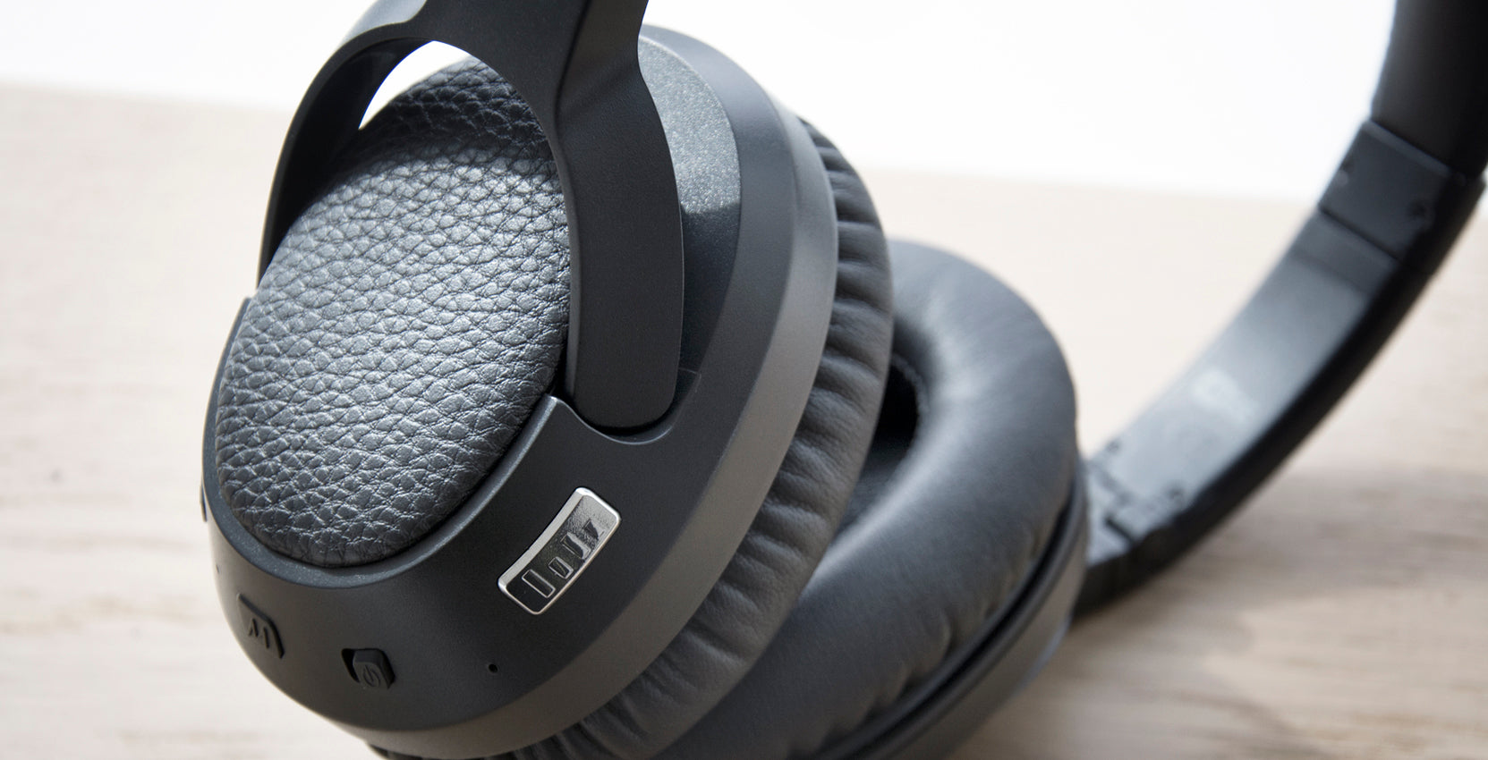Close-up of a black over-ear headphone resting on a wooden surface, focusing on the textured ear cushion and side controls.