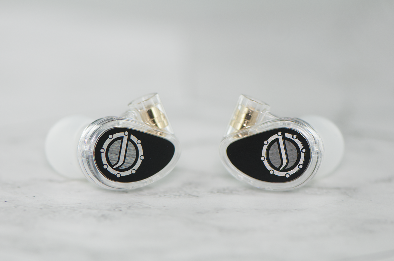 Two high-end in-ear monitors with transparent housings and black faceplates featuring a unique silver and white design, positioned on a marble surface.