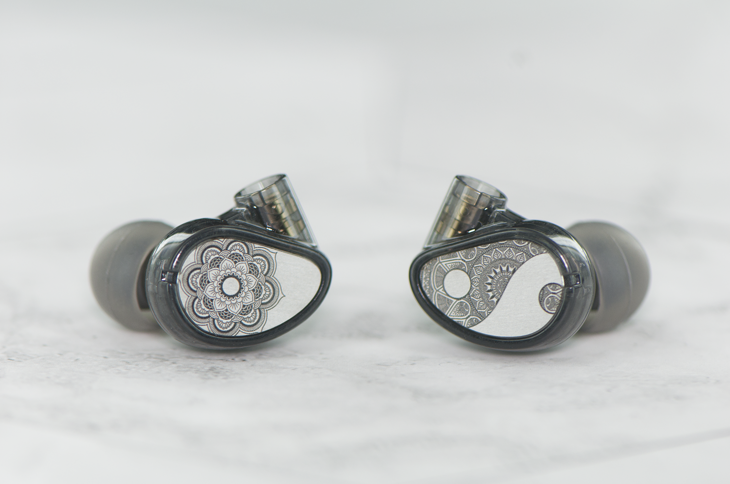 Two in-ear monitors with decorative silver and black floral designs on a white marble background.