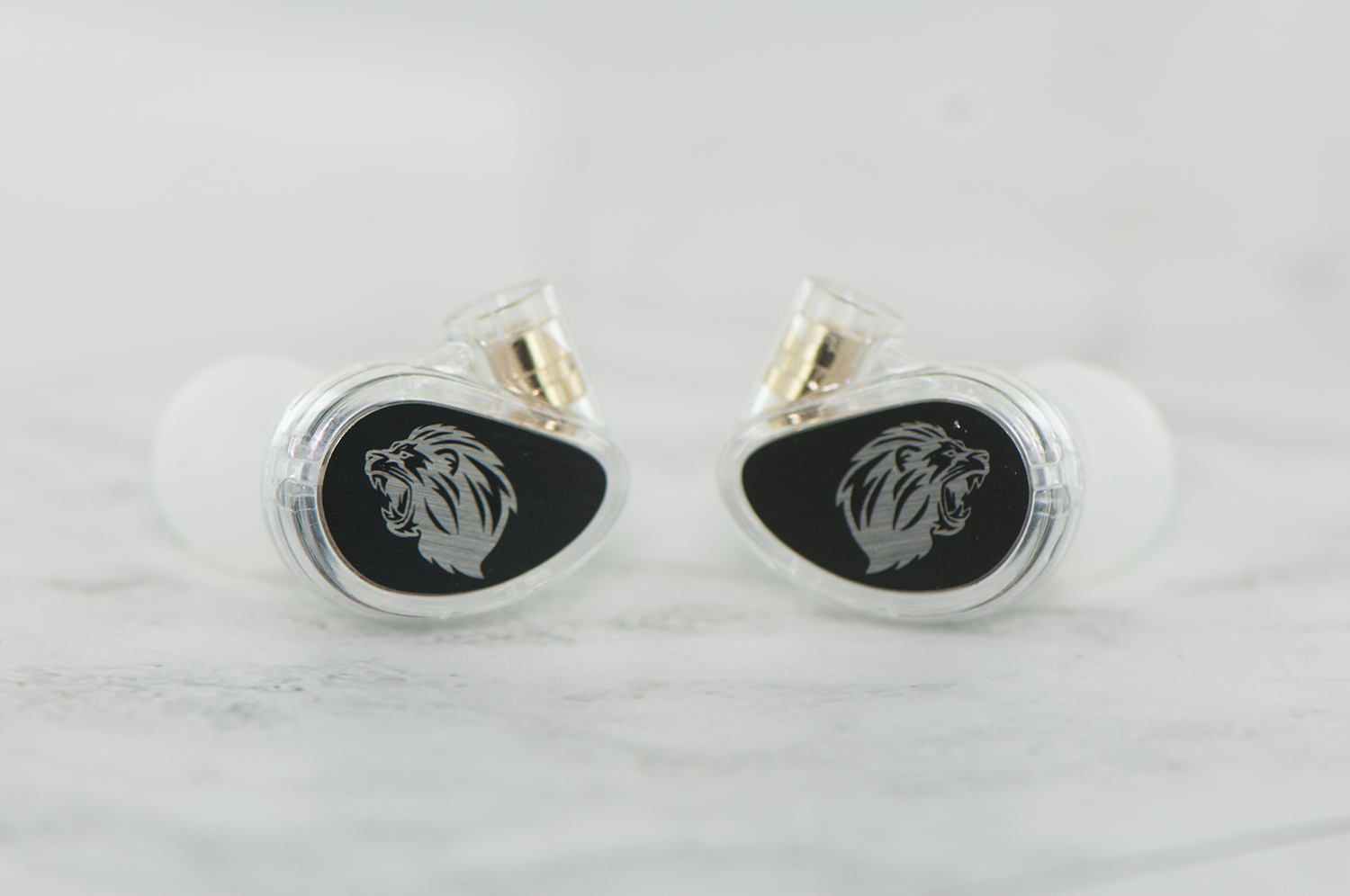 Two high-end in-ear monitors with a lion emblem on a black background, displayed on a marble surface.