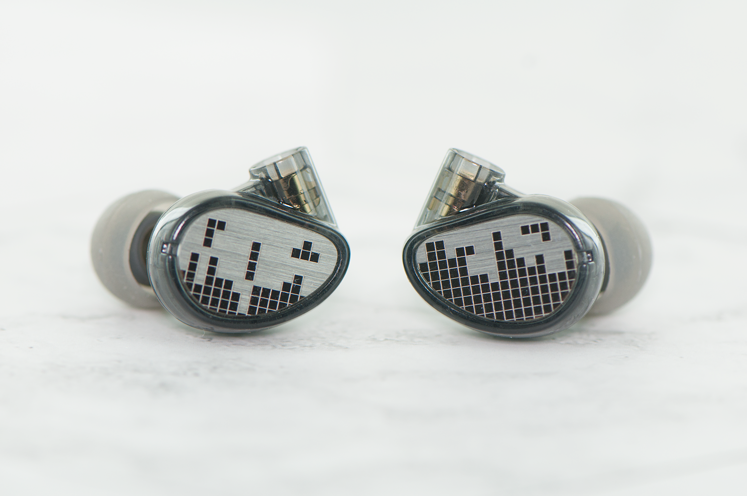 Two high-end, black and silver in-ear monitors with a unique hexagonal design and shiny metallic finish, set against a white background.