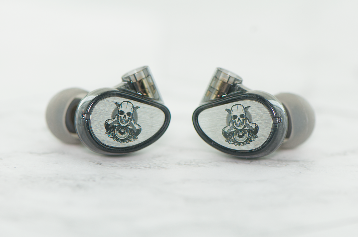 Two high-end in-ear monitors with a skull design on a transparent casing, placed on a white surface.