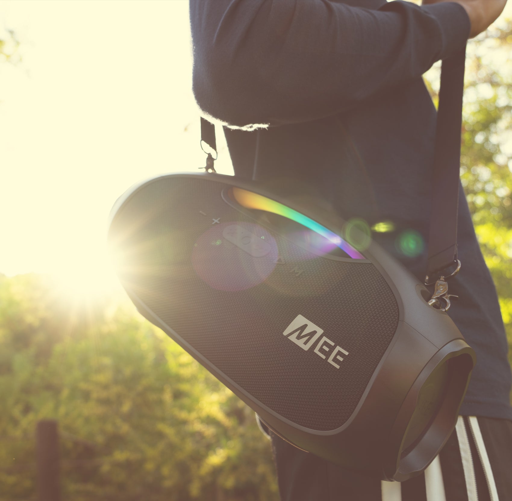 A person holding a portable meg speaker over their shoulder outdoors, with sunlight creating a lens flare.