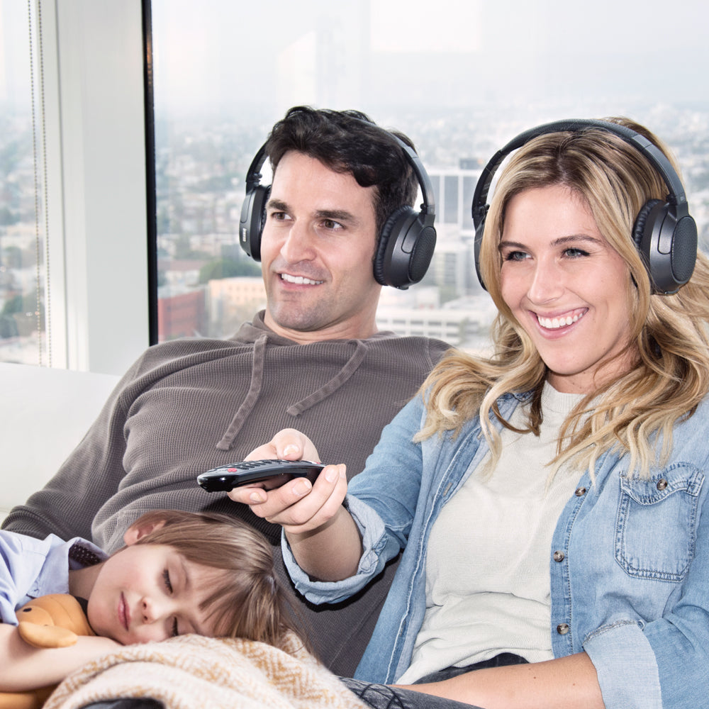 Family sitting together with headphones on, watching TV with a sleeping child 