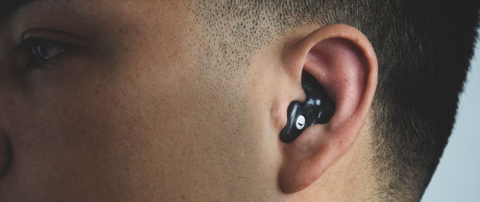 Close-up of the side of a person's face showing an ear with a black wireless earbud.