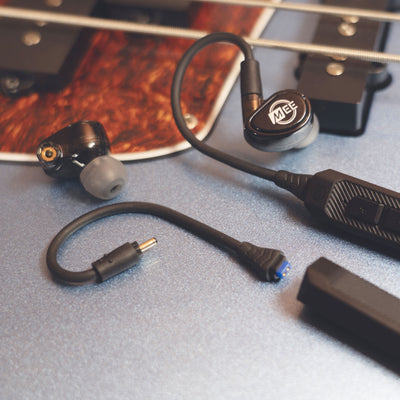 Black MEE audio MX2 PRO Musicians' In-Ear Monitors and a BT3 Hi-Res Bluetooth Audio Adapter displayed on a guitar. 