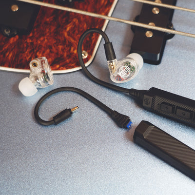 Clear MEE audio MX1 PRO Musicians' In-Ear Monitors and BT3 Hi-Res Bluetooth Audio Adapter displayed on a guitar. 