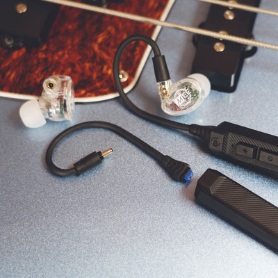 Clear MEE audio MX2 PRO Musicians' In-Ear Monitors and a BT3 Hi-Res Bluetooth Audio Adapter displayed on a guitar. 