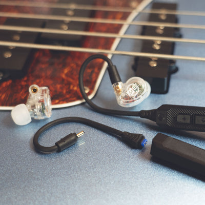 Clear MEE audio MX2 PRO Musicians' In-Ear Monitors and a BT3 Hi-Res Bluetooth Audio Adapter displayed on a guitar. 