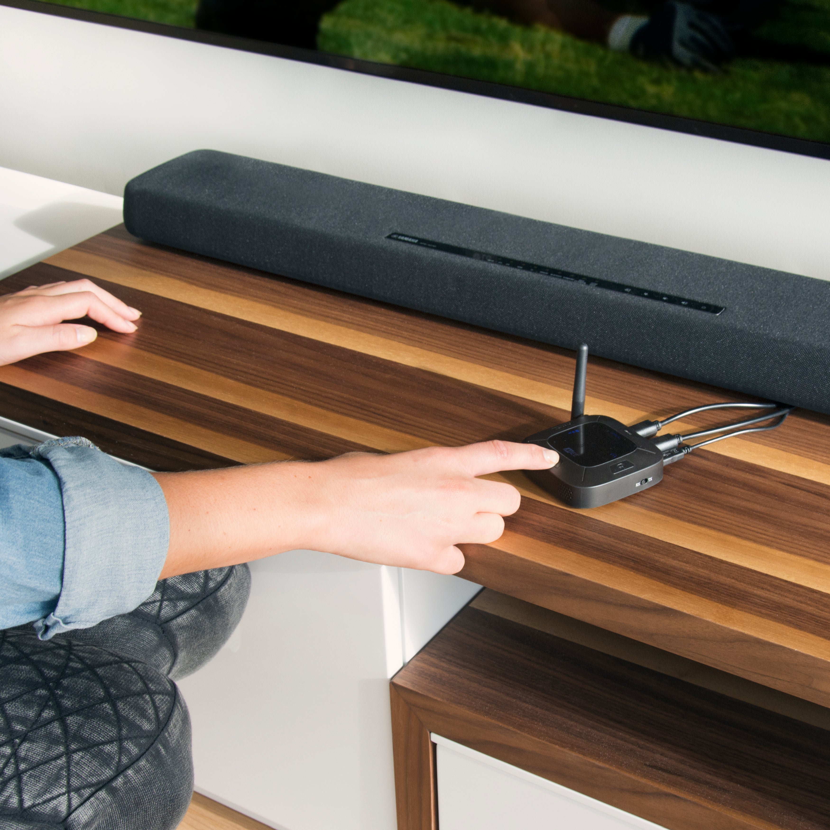 Person adjusting a Connect HUB on a wooden table with a TV and Soundbar in the background