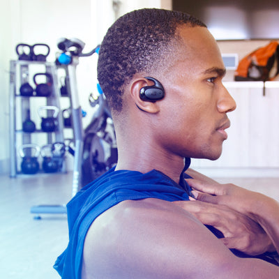 Man wearing a blue tank top and AirHook Pro earbud in a gym setting