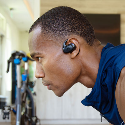 Man wearing a AirHook Pro earbud in an indoor setting with a bicycle in the background